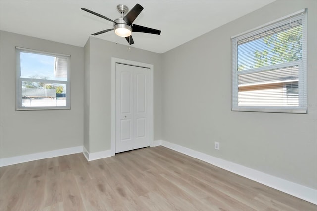 unfurnished bedroom featuring multiple windows, ceiling fan, a closet, and light wood-type flooring