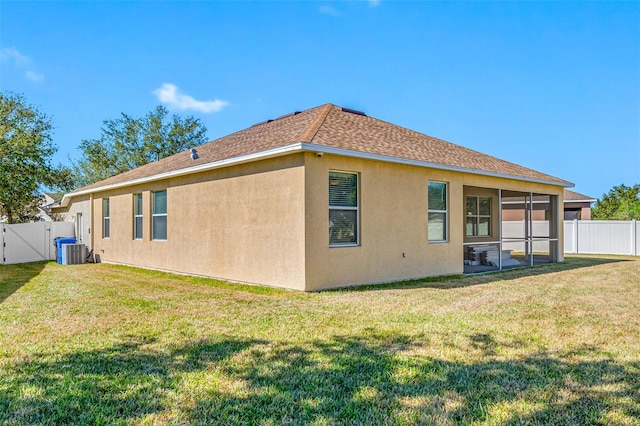 rear view of house with central AC unit, a sunroom, and a yard