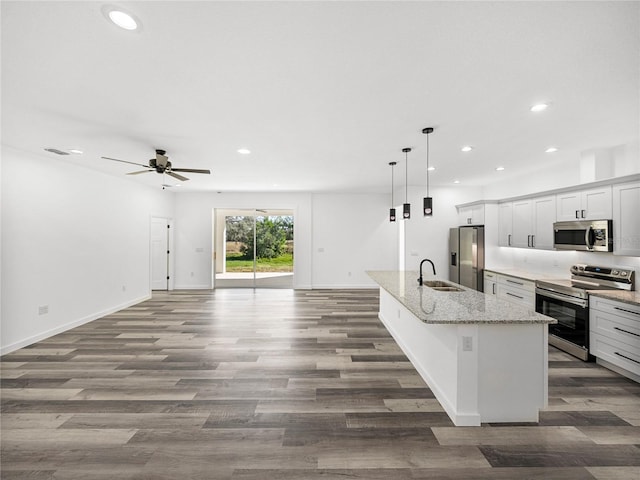 kitchen with light stone countertops, appliances with stainless steel finishes, decorative light fixtures, an island with sink, and sink