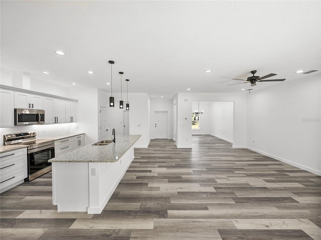 kitchen featuring pendant lighting, appliances with stainless steel finishes, sink, light stone countertops, and an island with sink