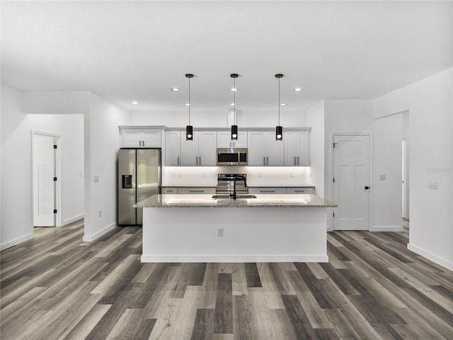 kitchen featuring hanging light fixtures, appliances with stainless steel finishes, sink, light stone countertops, and a center island with sink