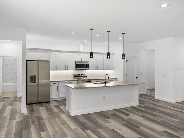 kitchen featuring pendant lighting, sink, light stone countertops, an island with sink, and stainless steel appliances