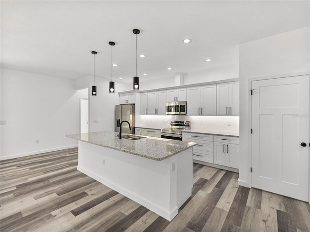 kitchen with decorative light fixtures, light wood-type flooring, light stone counters, an island with sink, and stainless steel appliances