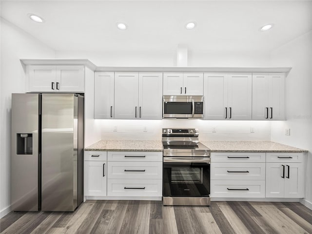 kitchen with white cabinets, dark hardwood / wood-style flooring, light stone countertops, and stainless steel appliances