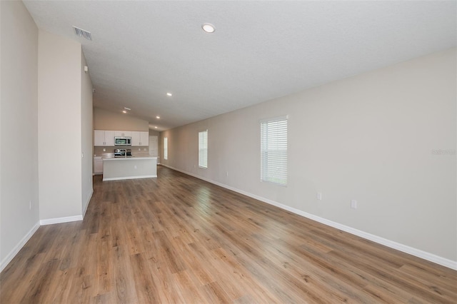 unfurnished living room with recessed lighting, visible vents, light wood-style flooring, vaulted ceiling, and baseboards