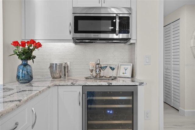 kitchen featuring light stone countertops, wine cooler, backsplash, light hardwood / wood-style floors, and white cabinets