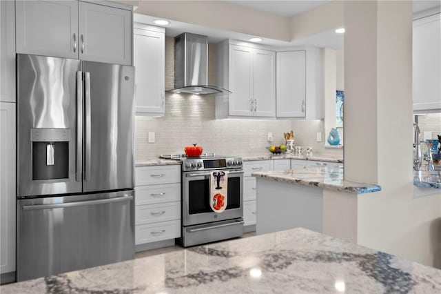 kitchen featuring wall chimney range hood, decorative backsplash, appliances with stainless steel finishes, light stone counters, and white cabinetry