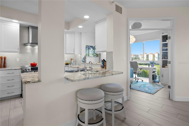 kitchen featuring kitchen peninsula, white cabinetry, light stone countertops, and wall chimney exhaust hood