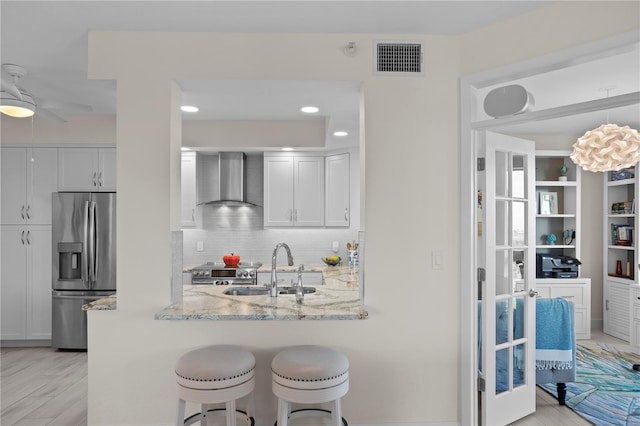 kitchen with white cabinets, wall chimney range hood, light hardwood / wood-style flooring, kitchen peninsula, and stainless steel appliances