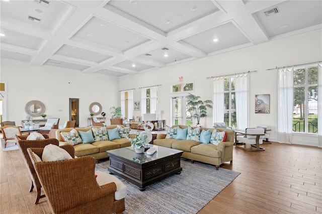 living room with a towering ceiling, beamed ceiling, light hardwood / wood-style floors, and coffered ceiling