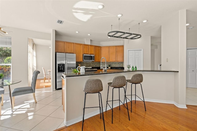 kitchen with kitchen peninsula, decorative backsplash, light wood-type flooring, and stainless steel appliances