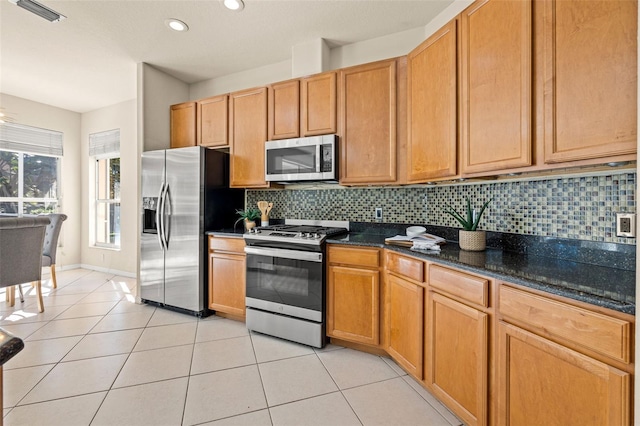 kitchen with light tile patterned flooring, backsplash, stainless steel appliances, and dark stone countertops