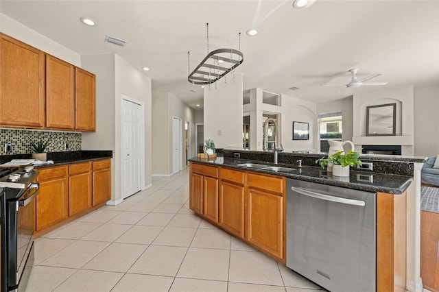 kitchen featuring sink, dark stone counters, light tile patterned flooring, ceiling fan with notable chandelier, and appliances with stainless steel finishes