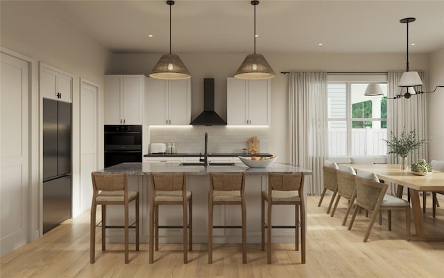 kitchen with wall chimney exhaust hood, light hardwood / wood-style floors, white cabinetry, and an island with sink