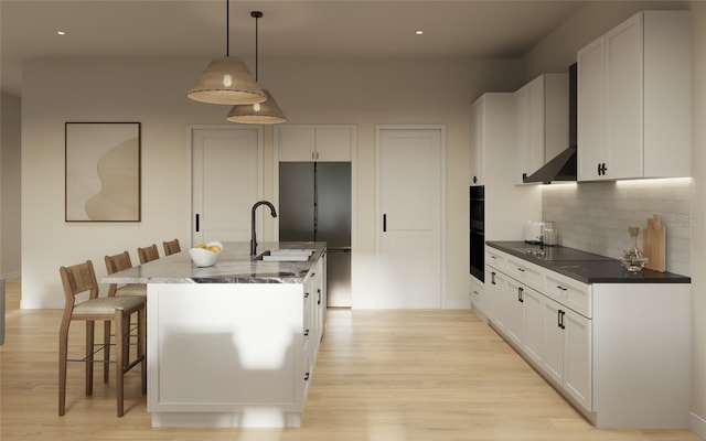 kitchen featuring a kitchen breakfast bar, decorative light fixtures, light hardwood / wood-style flooring, white cabinetry, and an island with sink