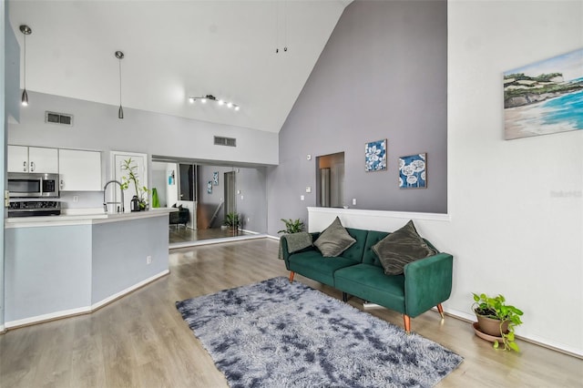 living room featuring high vaulted ceiling, light hardwood / wood-style floors, and sink