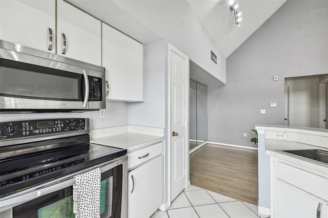 kitchen featuring white cabinetry, vaulted ceiling, light tile patterned flooring, and appliances with stainless steel finishes