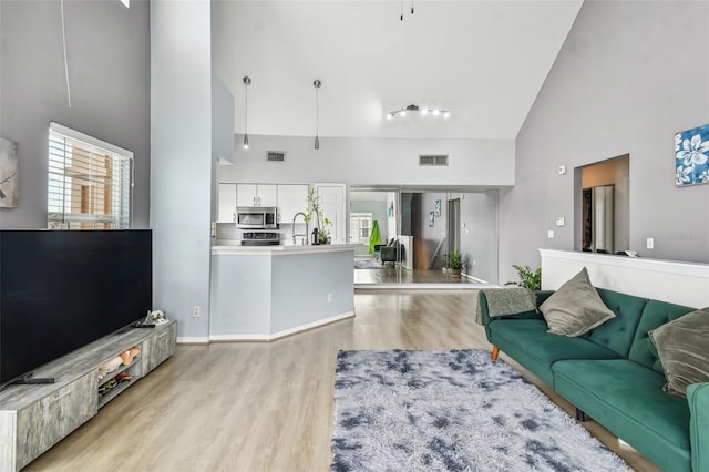 living room featuring sink, high vaulted ceiling, and light wood-type flooring