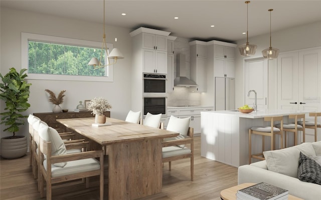 kitchen featuring pendant lighting, white cabinetry, wall chimney range hood, a kitchen island with sink, and a breakfast bar