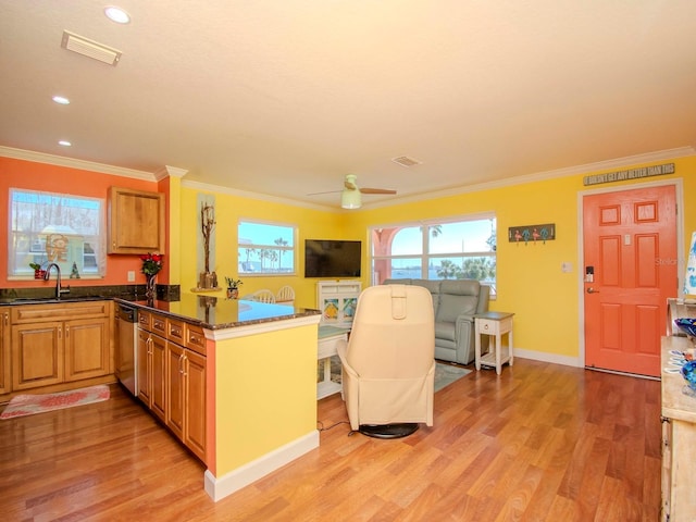 kitchen featuring sink, light wood-type flooring, stainless steel dishwasher, ornamental molding, and dark stone counters