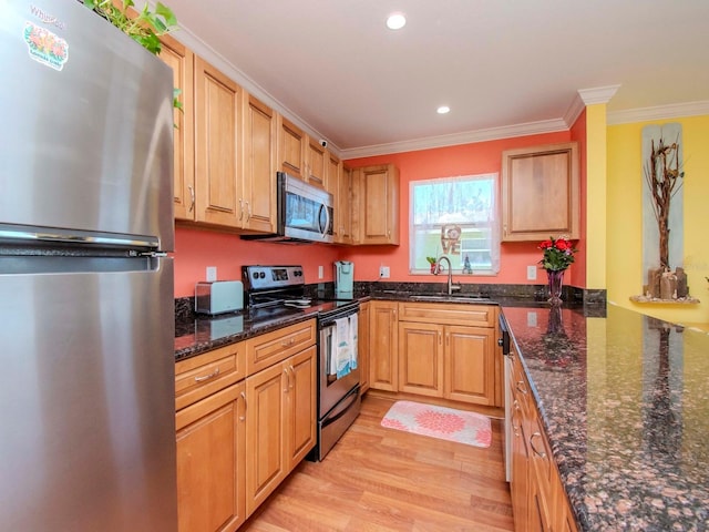 kitchen with sink, dark stone counters, ornamental molding, stainless steel appliances, and light wood-type flooring