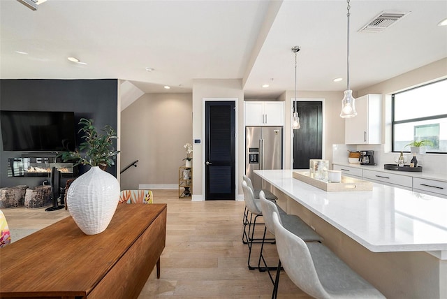 kitchen featuring pendant lighting, high end refrigerator, a kitchen island, light hardwood / wood-style floors, and white cabinetry