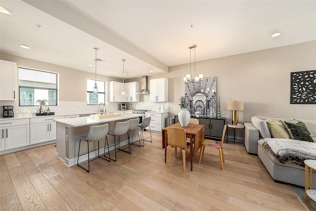 kitchen with wall chimney exhaust hood, light hardwood / wood-style floors, white cabinetry, and a kitchen island with sink