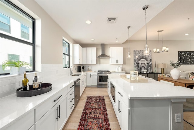 kitchen featuring white cabinetry, sink, stainless steel appliances, wall chimney range hood, and a kitchen island