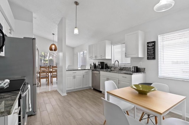 kitchen featuring white cabinets, stainless steel appliances, hanging light fixtures, and light hardwood / wood-style floors