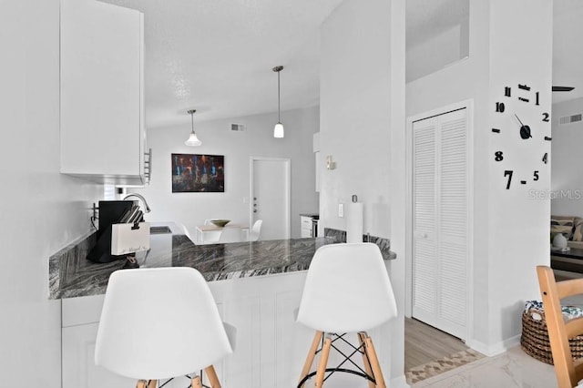 kitchen featuring white cabinetry, sink, hanging light fixtures, vaulted ceiling, and a breakfast bar