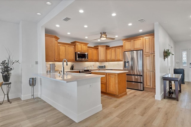 kitchen featuring a breakfast bar area, light hardwood / wood-style flooring, ceiling fan, kitchen peninsula, and stainless steel appliances