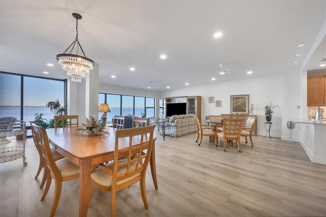 dining room featuring ceiling fan with notable chandelier, a water view, and light hardwood / wood-style flooring