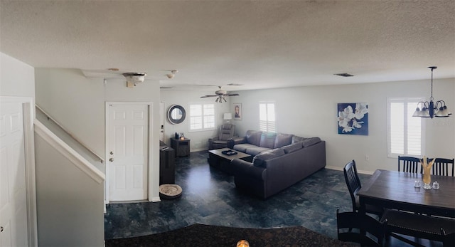 living room with ceiling fan with notable chandelier and a textured ceiling