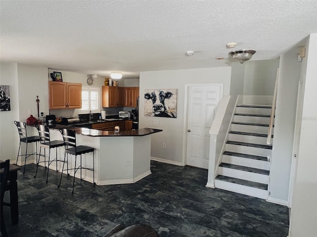 kitchen with brown cabinets, a breakfast bar area, dark countertops, a sink, and a peninsula