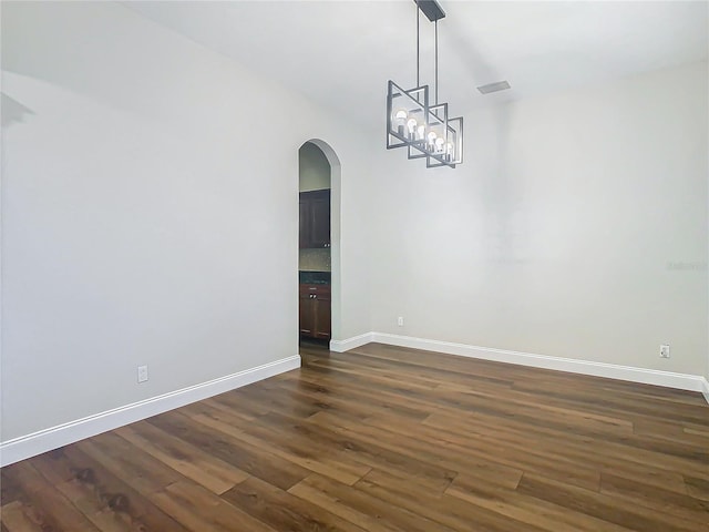 empty room with dark wood-type flooring and a notable chandelier