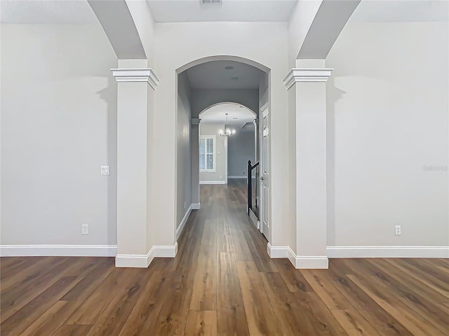 hall featuring decorative columns, dark wood-type flooring, and an inviting chandelier