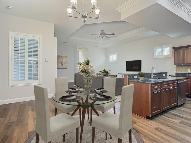 dining area with ceiling fan with notable chandelier, a raised ceiling, sink, light wood-type flooring, and ornamental molding