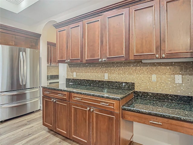 kitchen with backsplash, light hardwood / wood-style flooring, stainless steel refrigerator, and dark stone countertops