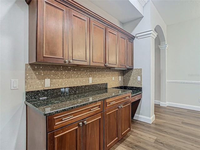 kitchen with light hardwood / wood-style floors, ornate columns, backsplash, and dark stone counters