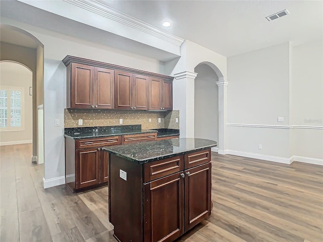 kitchen featuring dark stone countertops, wood-type flooring, dark brown cabinetry, and tasteful backsplash