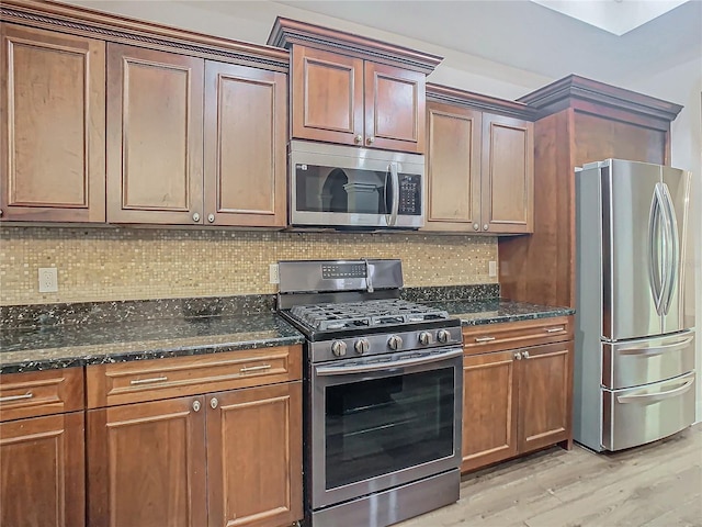 kitchen with decorative backsplash, appliances with stainless steel finishes, light hardwood / wood-style floors, and dark stone countertops