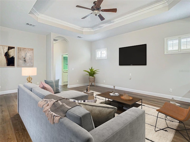 living room with ceiling fan, dark hardwood / wood-style flooring, crown molding, and a tray ceiling