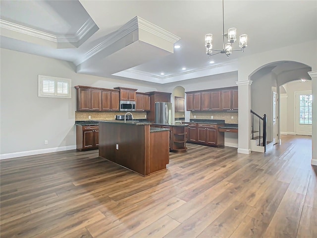 kitchen featuring decorative backsplash, appliances with stainless steel finishes, a kitchen island with sink, and dark wood-type flooring