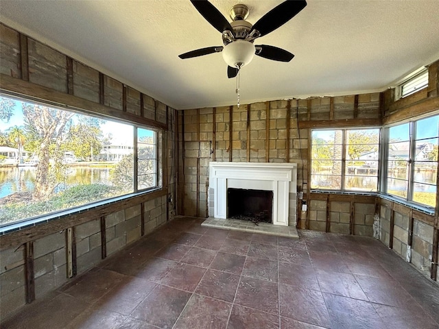 unfurnished living room featuring ceiling fan, a water view, and a textured ceiling