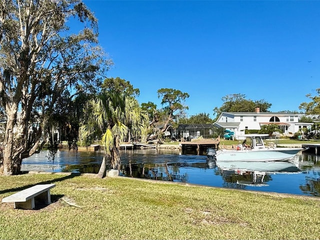 view of dock with a lanai, a water view, and a lawn