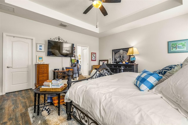 bedroom with a raised ceiling, ceiling fan, and dark wood-type flooring