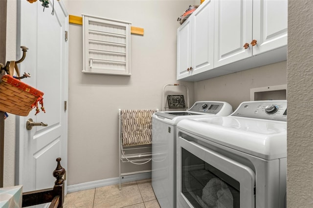 laundry room featuring washing machine and clothes dryer, light tile patterned floors, and cabinets