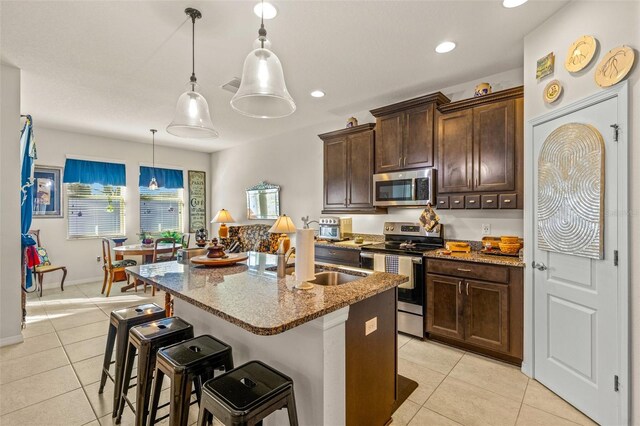 kitchen featuring sink, an island with sink, decorative light fixtures, light stone counters, and stainless steel appliances