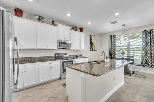 kitchen with sink, appliances with stainless steel finishes, dark stone countertops, white cabinets, and a center island with sink