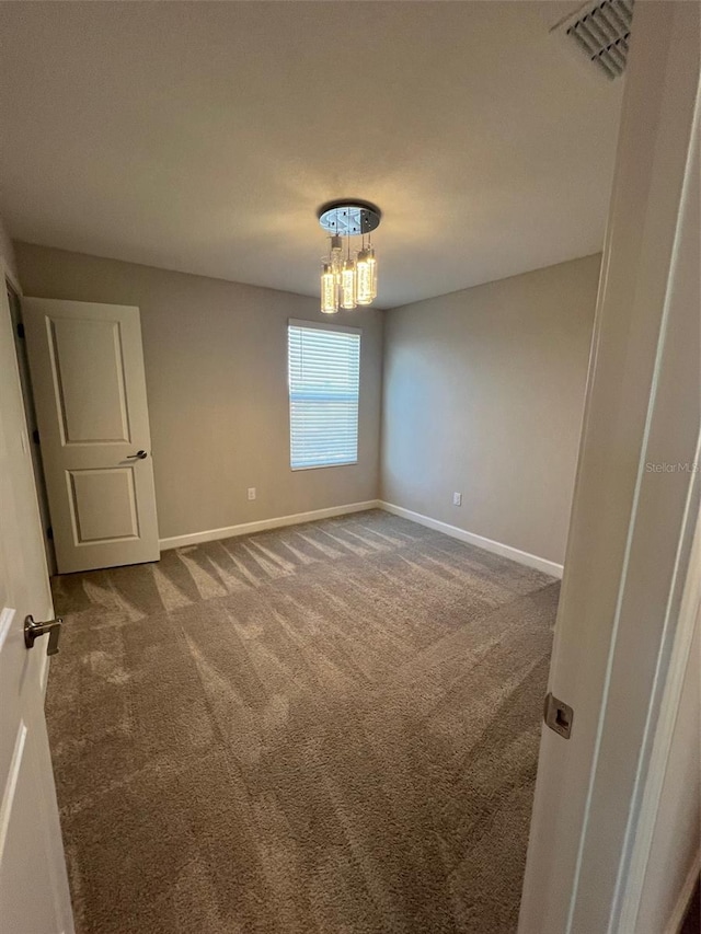 carpeted empty room with an inviting chandelier